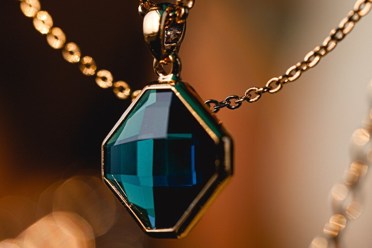 close up image of a teal blue gemstone necklace in a yellow gold setting