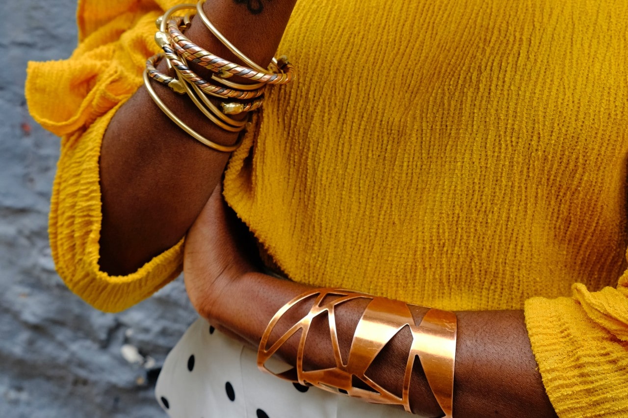 Close up image of a person in a yellow top with a number of gold bracelets on their wrists