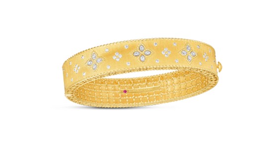 A wide, gold bangle by Roberto Coin with diamond details and a hidden ruby inlay