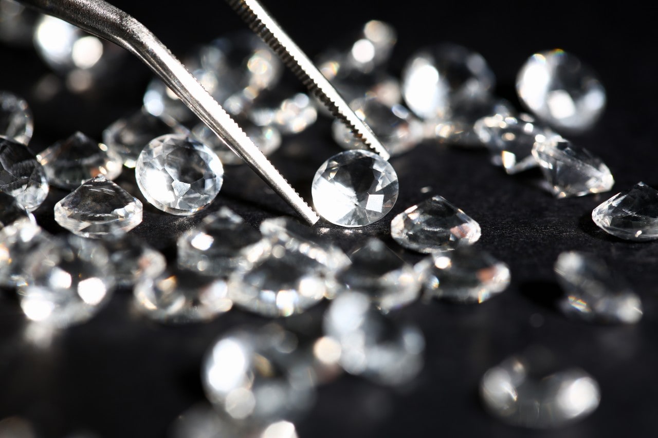 Several round cut diamonds. One diamond, held up by calipers, is being inspected