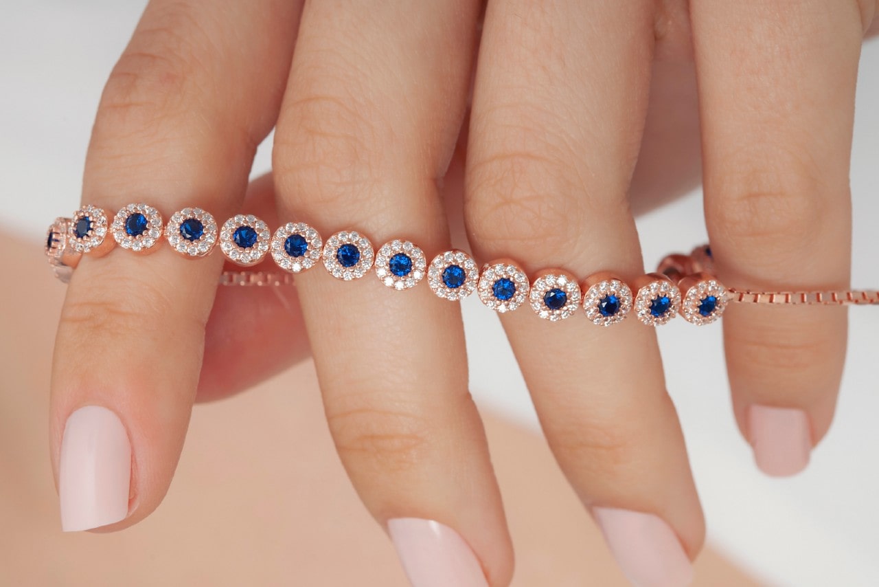 Close up image of a hand holding a rose gold bracelet featuring sapphires and diamonds