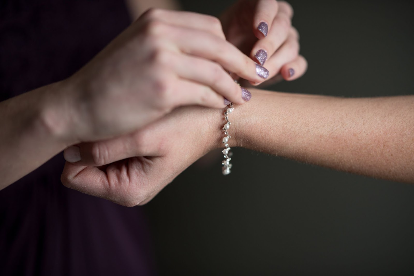 Close up of a woman putting a pearl and silver bracelet onto another woman’s wrist