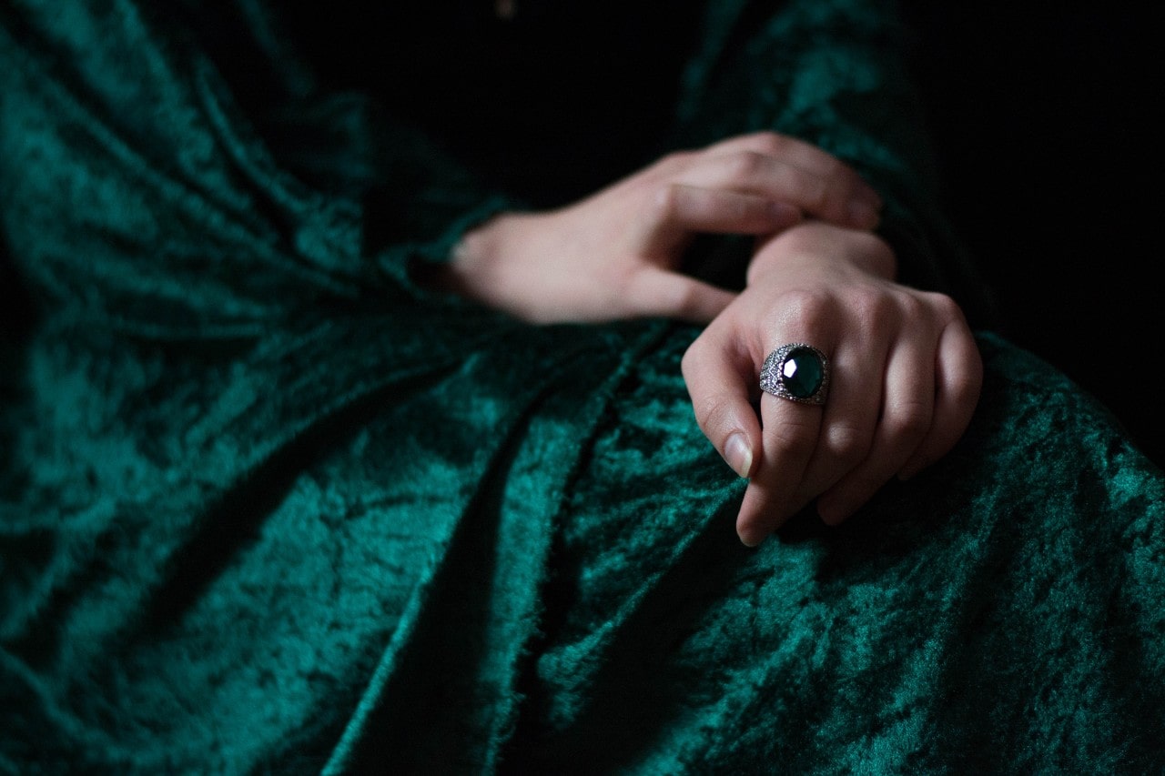 A woman bundled up in dark green velvet wears an emerald cocktail ring.