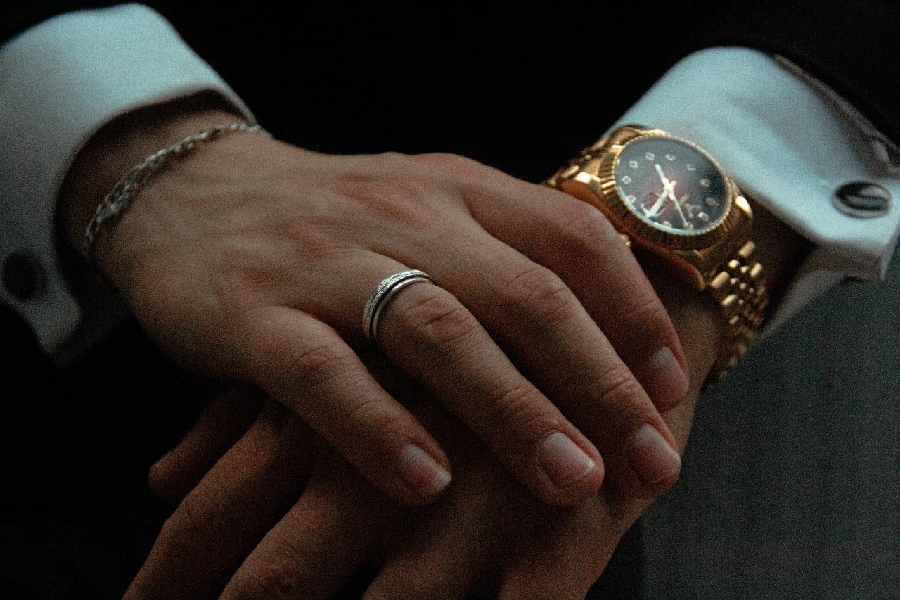 close-up of man’s hands clasped, a watch on one hand and a ring on the other