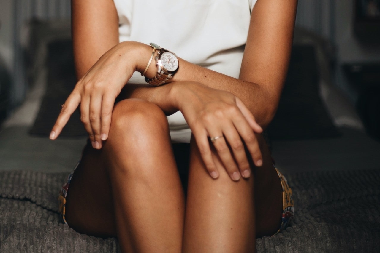 lady’s torso with her legs and arms crossed, wearing a luxury watch