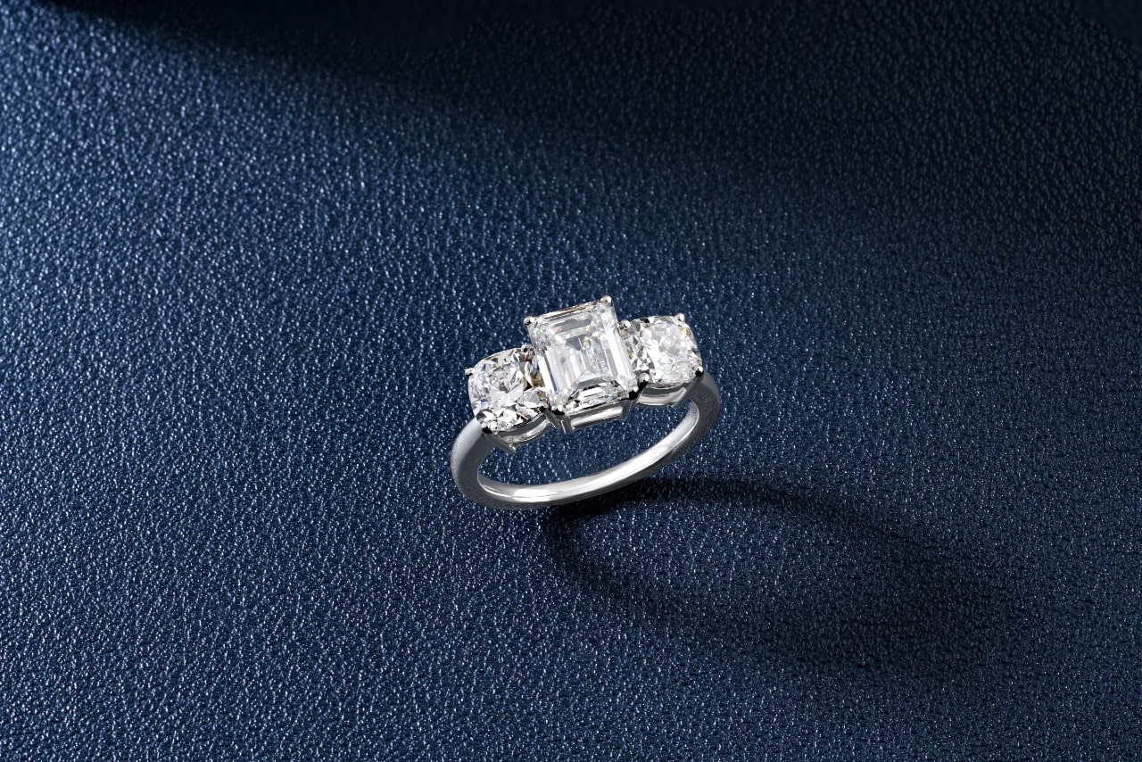 a three-stone engagement ring featuring an emerald cut center stone and two cushion cut side stones
