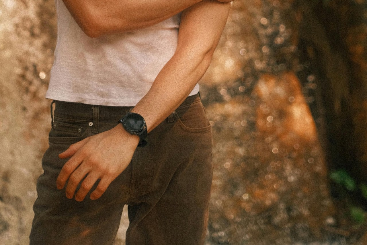 a man standing in a white shirt and brown pants wearing an all-black watch
