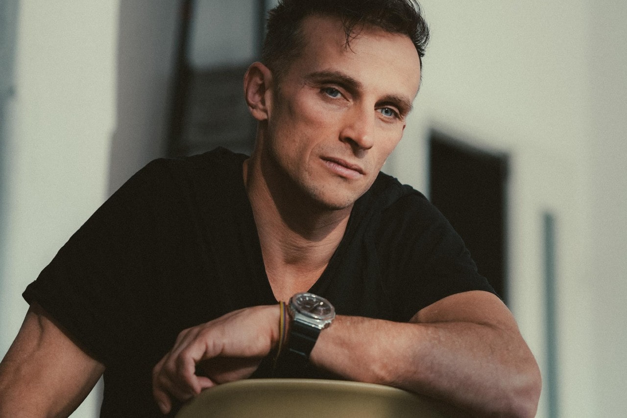 a man sitting backwards in a chair wearing a black shirt and black watch