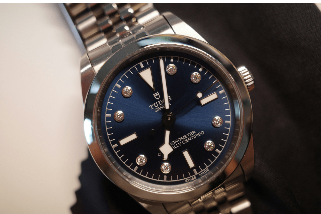 A close-up of a TUDOR dress watch with a navy blue dial, featuring diamond indices at 1, 2, 4, 5, 7, 8, 10, and 11.
