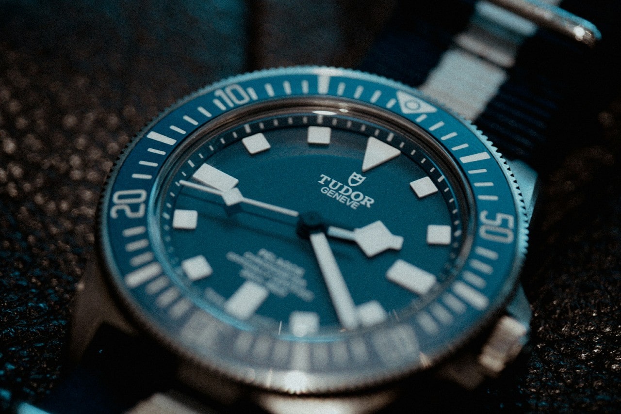 An extreme close-up of a sporty TUDOR watch with a blue dial and fabric strap displayed atop a bumpy leather surface.