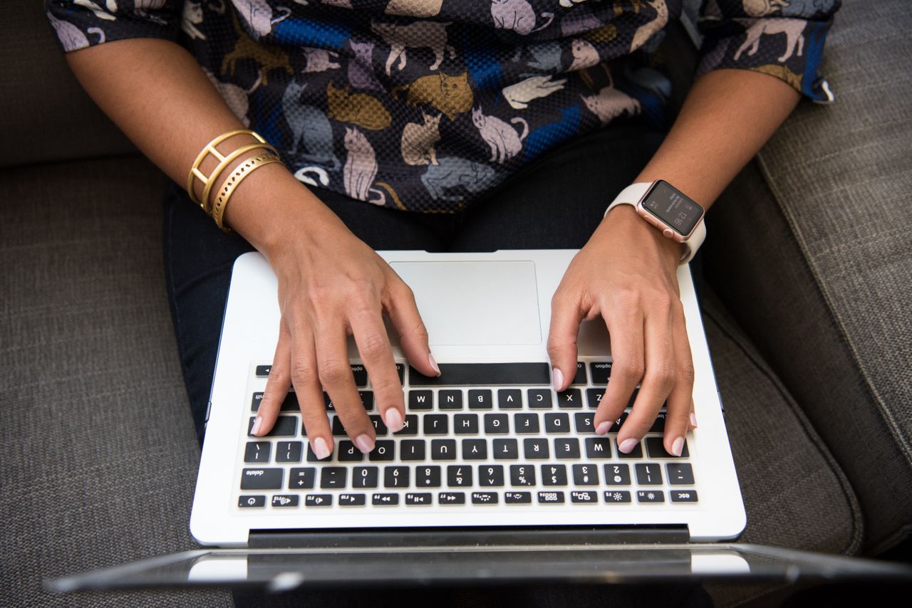 Person with gold bracelets and a watch types words on a laptop.
