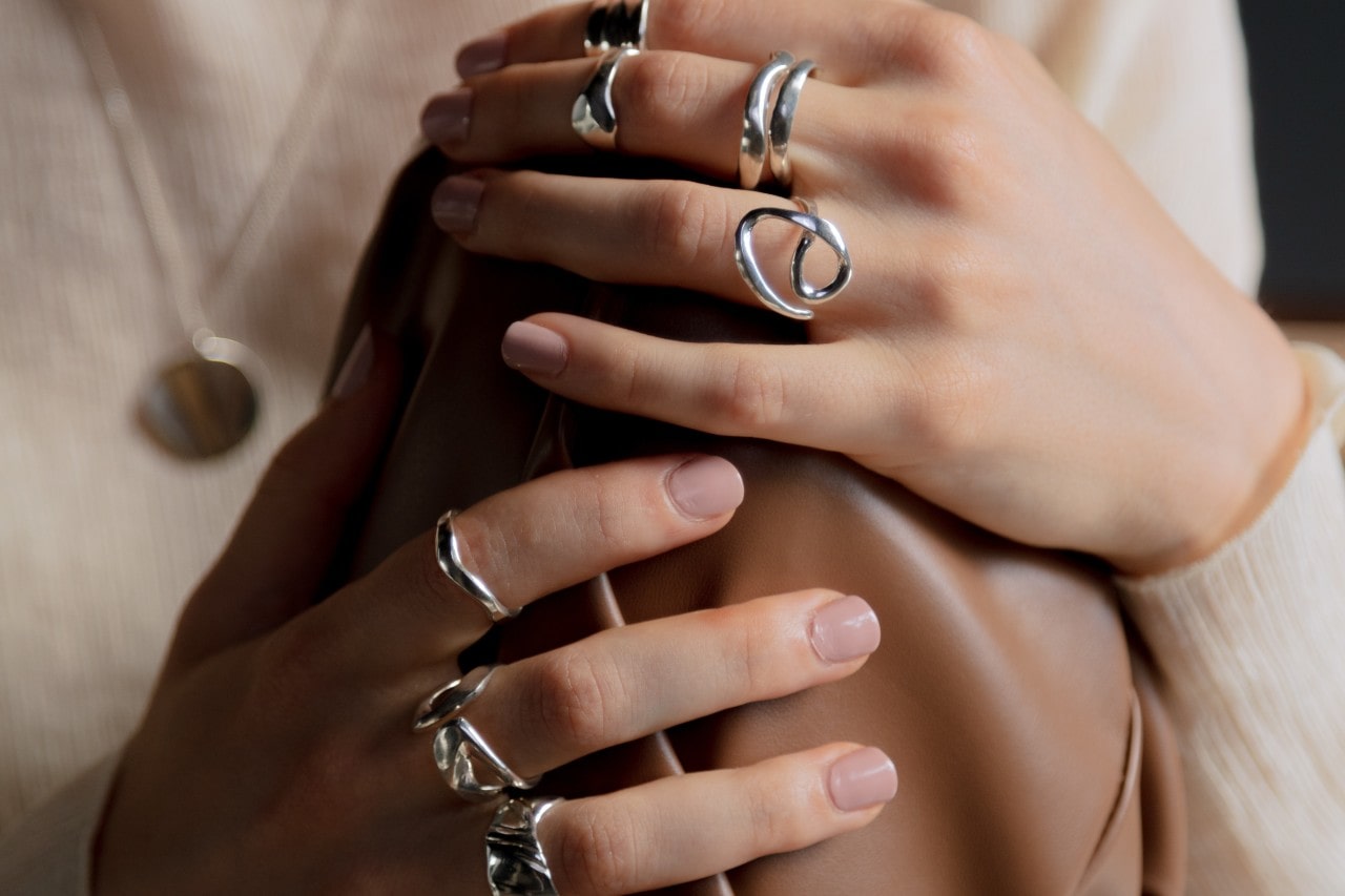 Two hands clad in numerous sterling silver fashion rings.