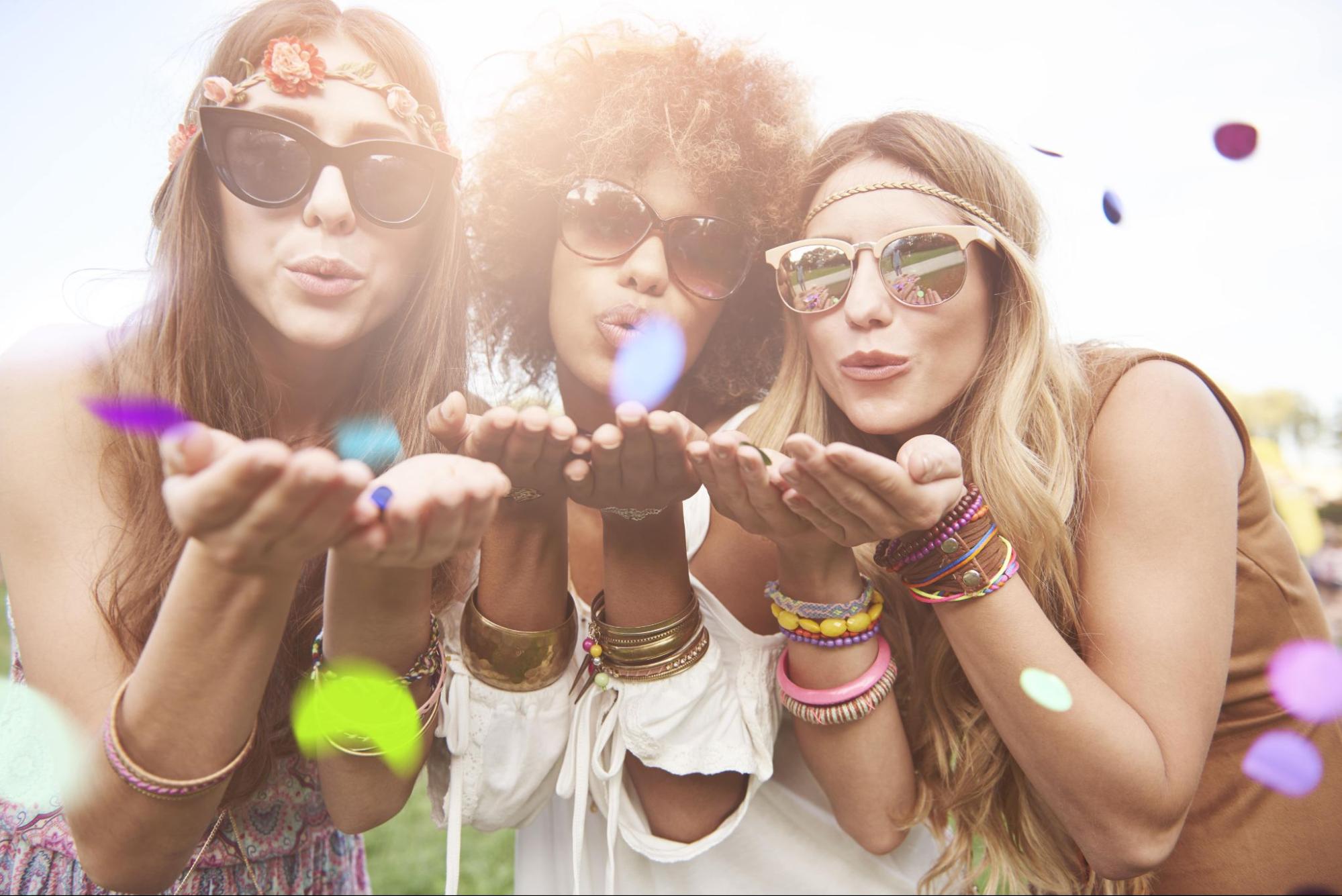 three women at a festival blowing confetti into the camera