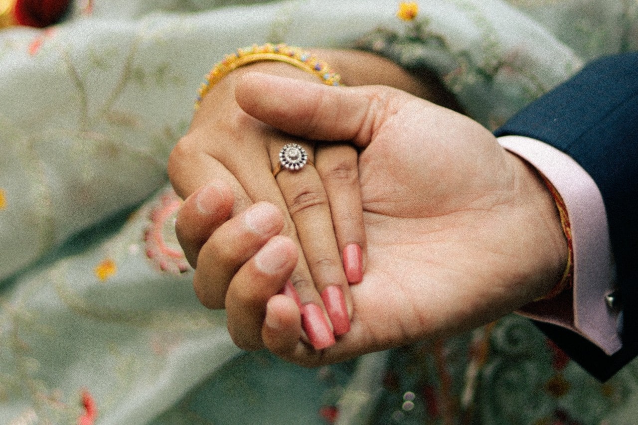 a man holds a woman’s hand, showing off her halo engagement ring.