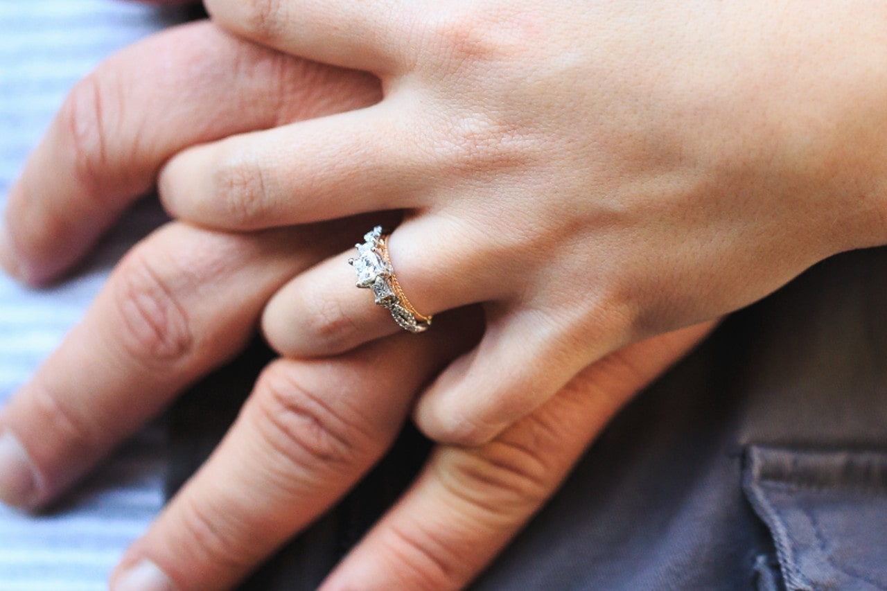 A woman holding a man’s hand wears a two-stone three stone ring.
