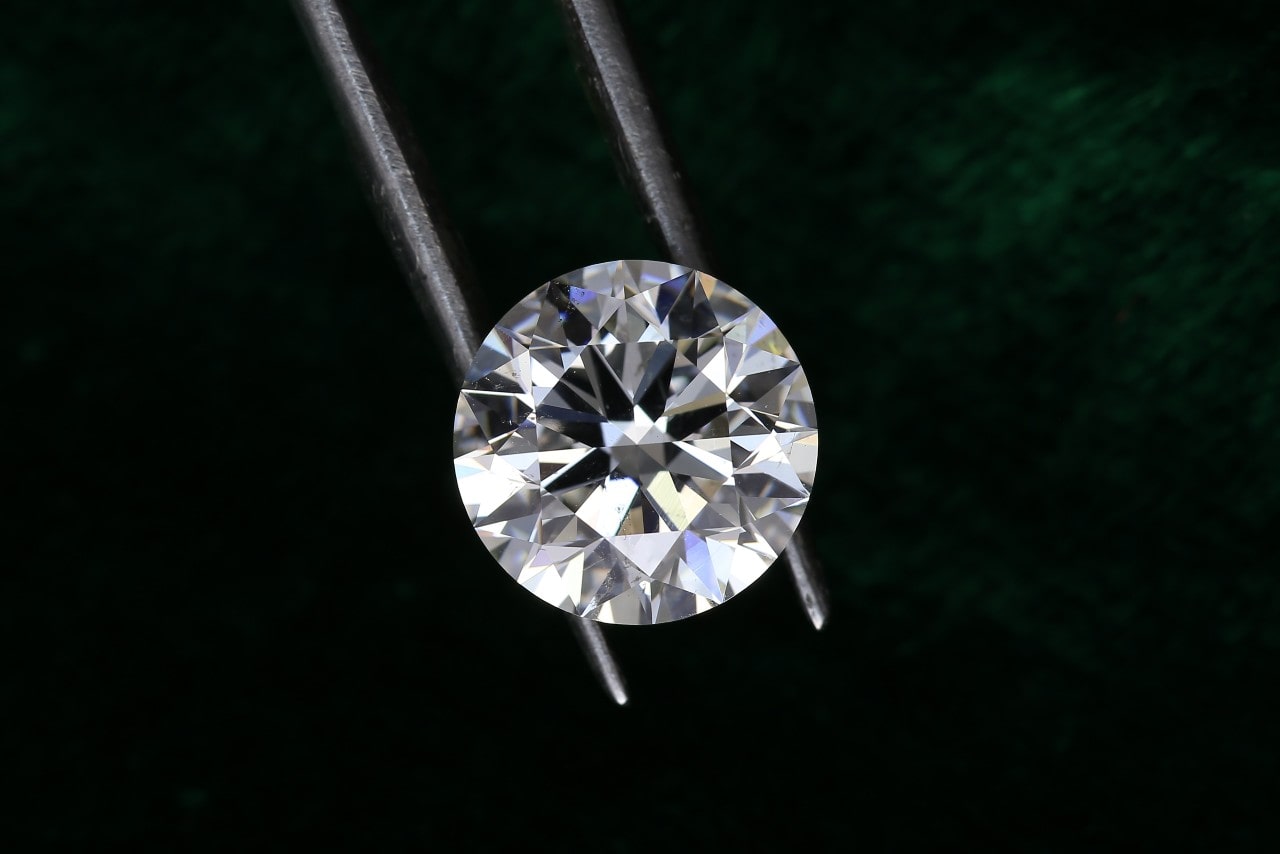 a round cut diamond held by tweezers against a black background