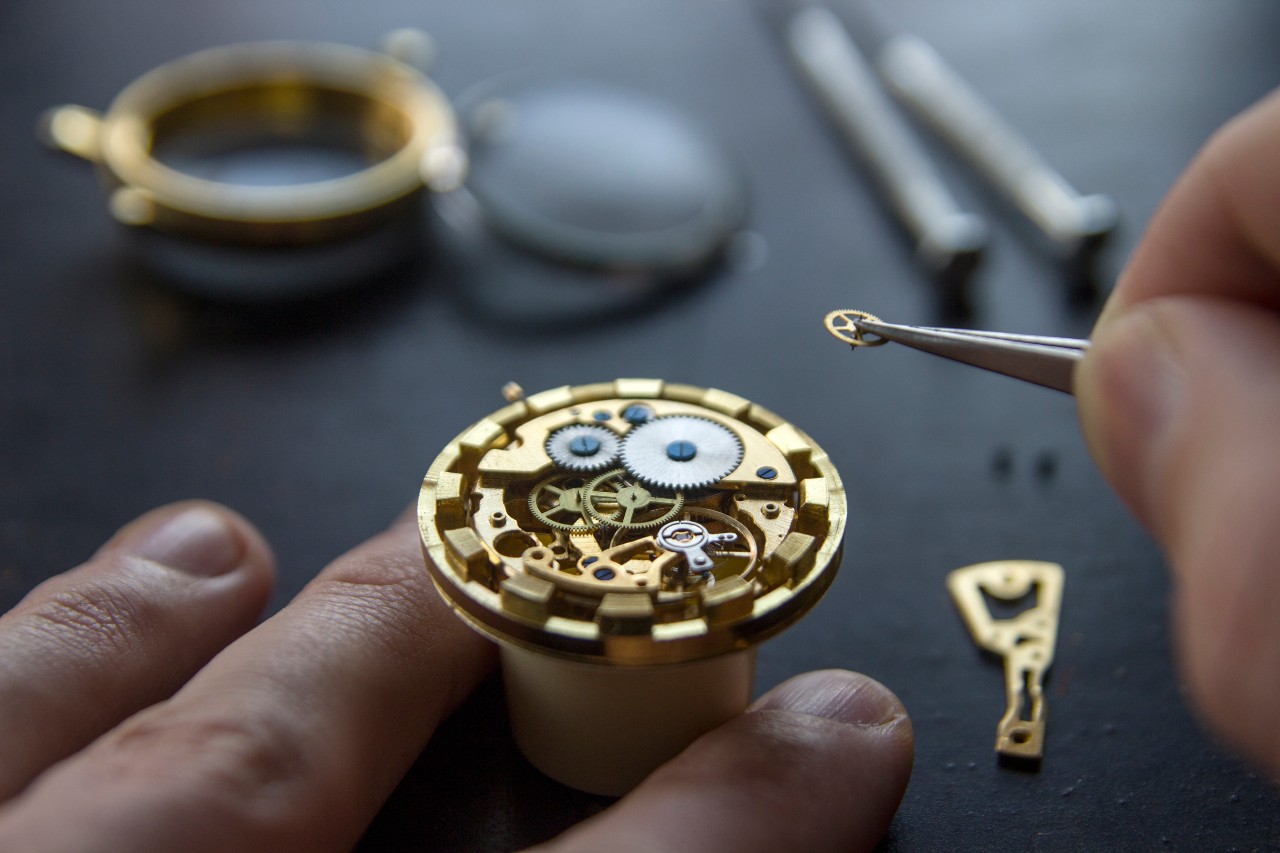 A close-up of a watchmaker maintaining a mechanical watch using precision tweezers.