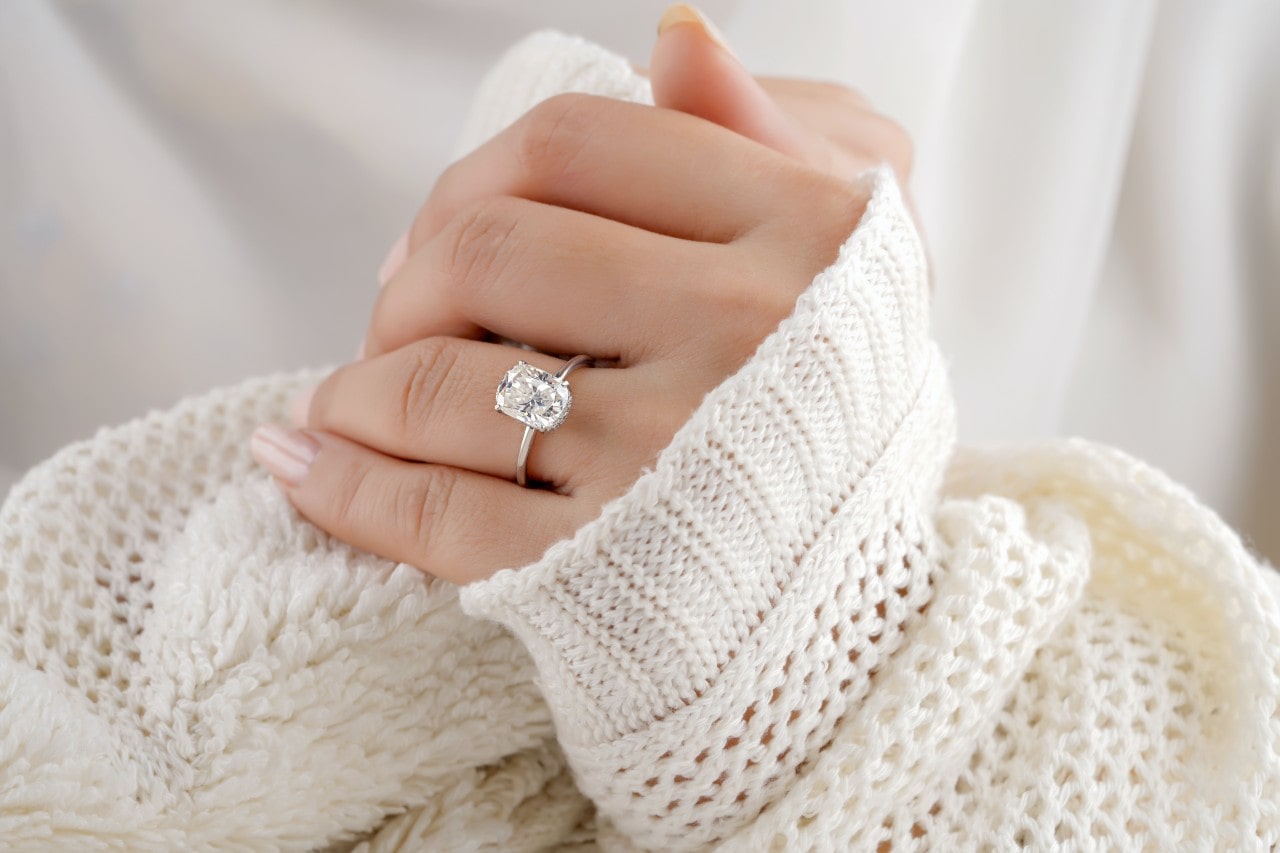A woman wearing a sweater wears a solitaire oval-cut diamond engagement ring.