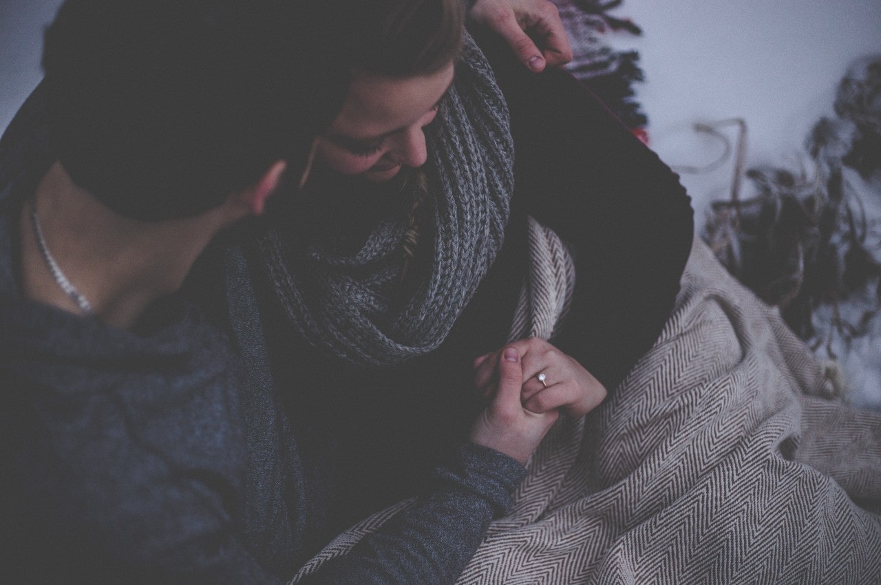 A couple snuggles together while admiring the engagement ring after a proposal.