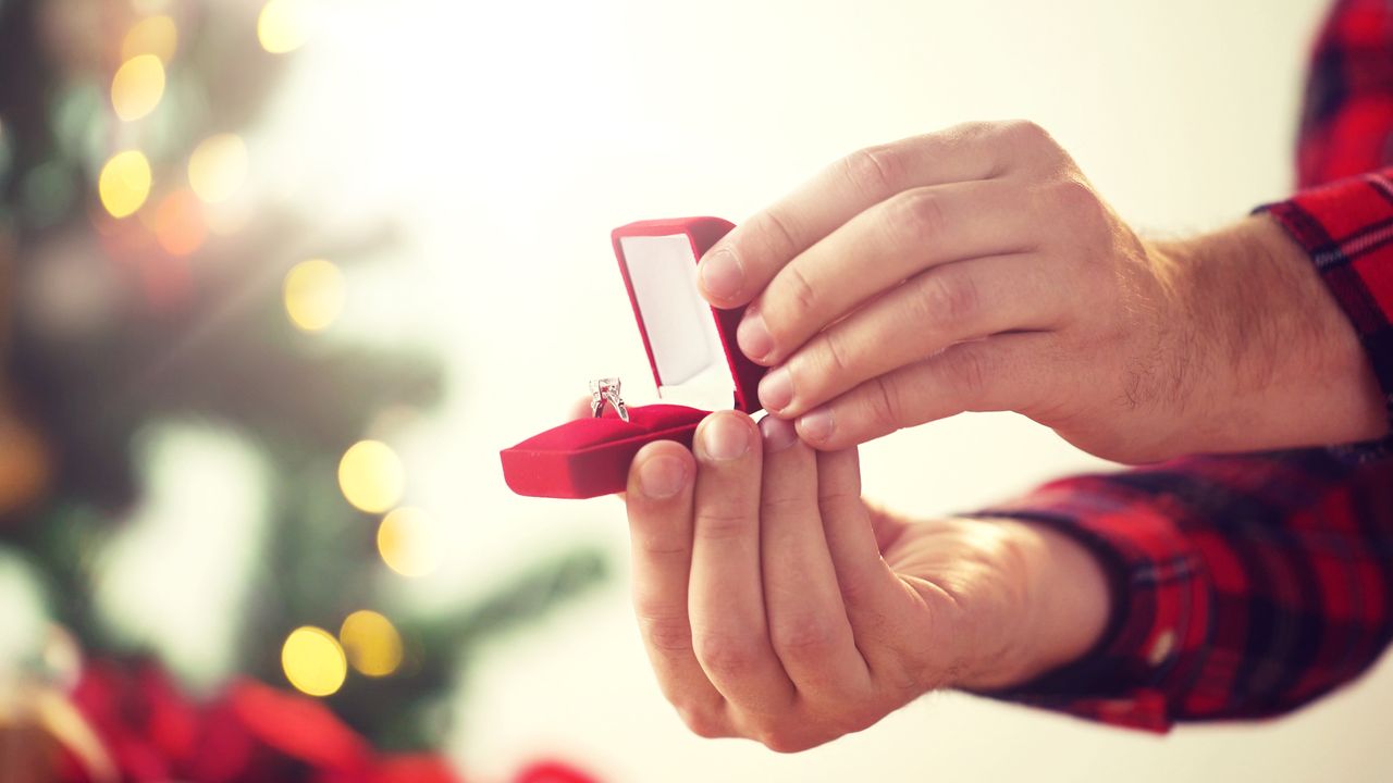 A man in flannel pajamas proposes on Christmas morning in front of the tree.
