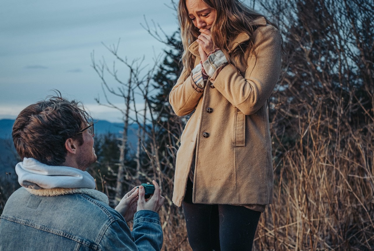 A man proposes to his girlfriend during a winter hike as the sun sets.
