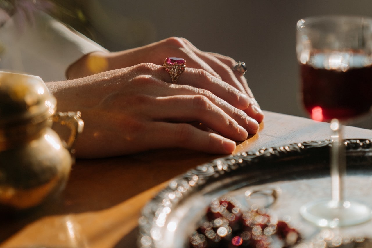 a woman’s hands resting on a lavish table and wearing gemstone rings