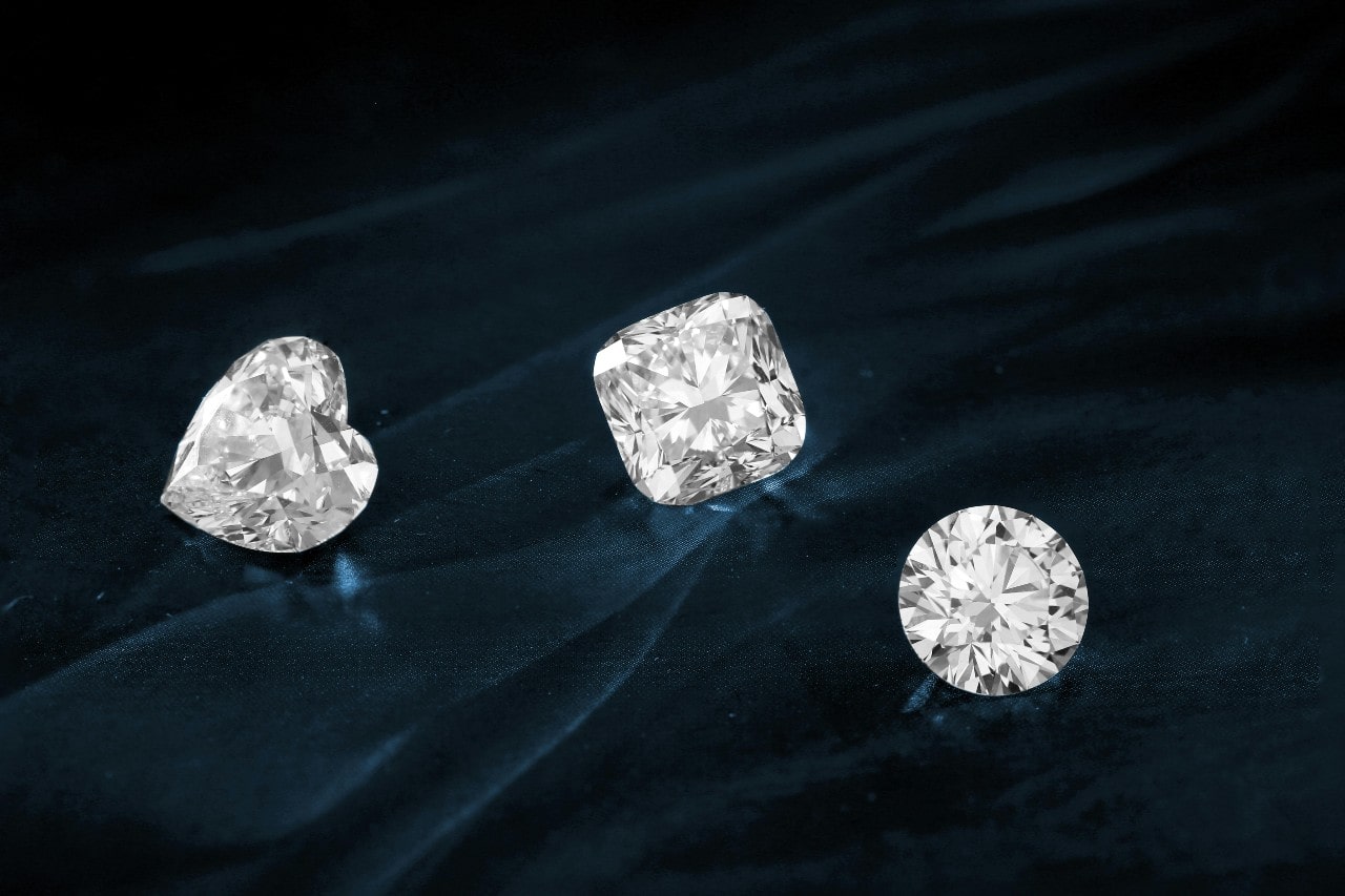 A heart-shaped, round-cut, and cushion-cut diamond placed on a dark green surface.