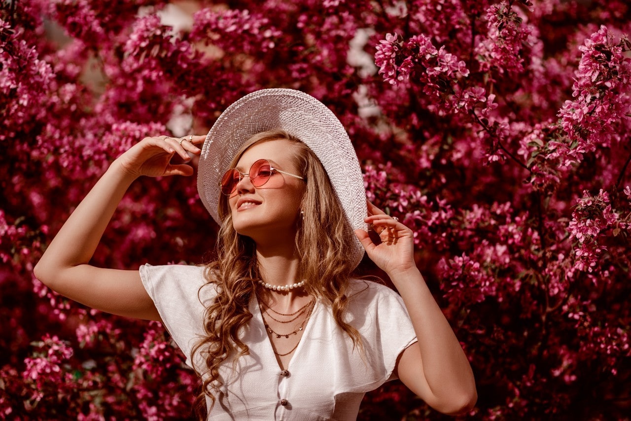 Woman standing in front of blooming flowers wearing multiple necklaces