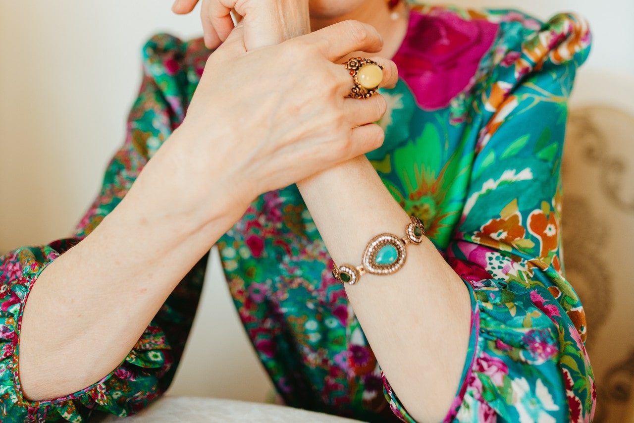 a woman in a brightly colored blouse, wearing a turquoise bracelet and gemstone ring.