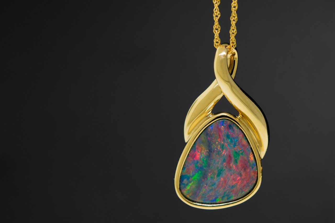 a gold pendant necklace with a multicolored gem.