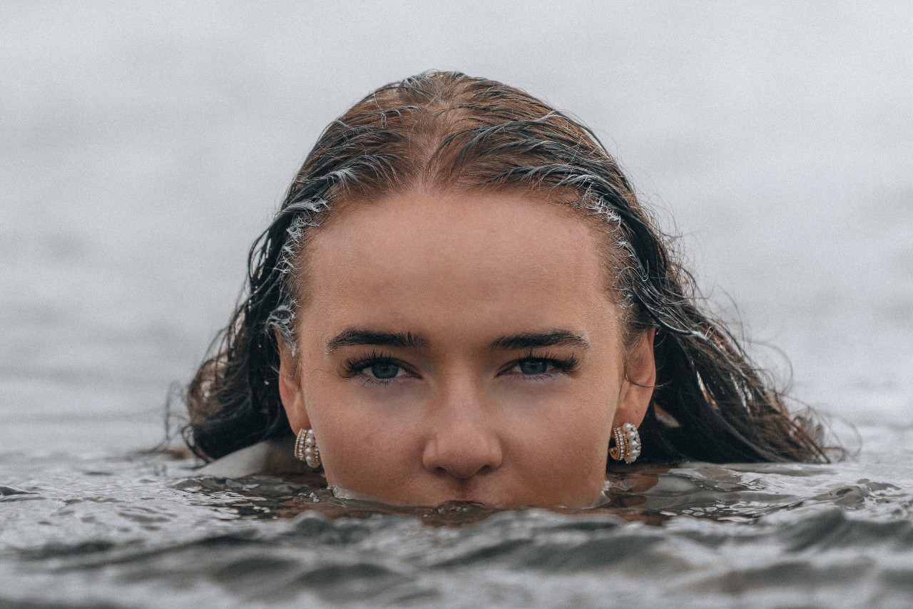a woman whose face is halfway underwater and is wearing a pair of gold hoop earrings.
