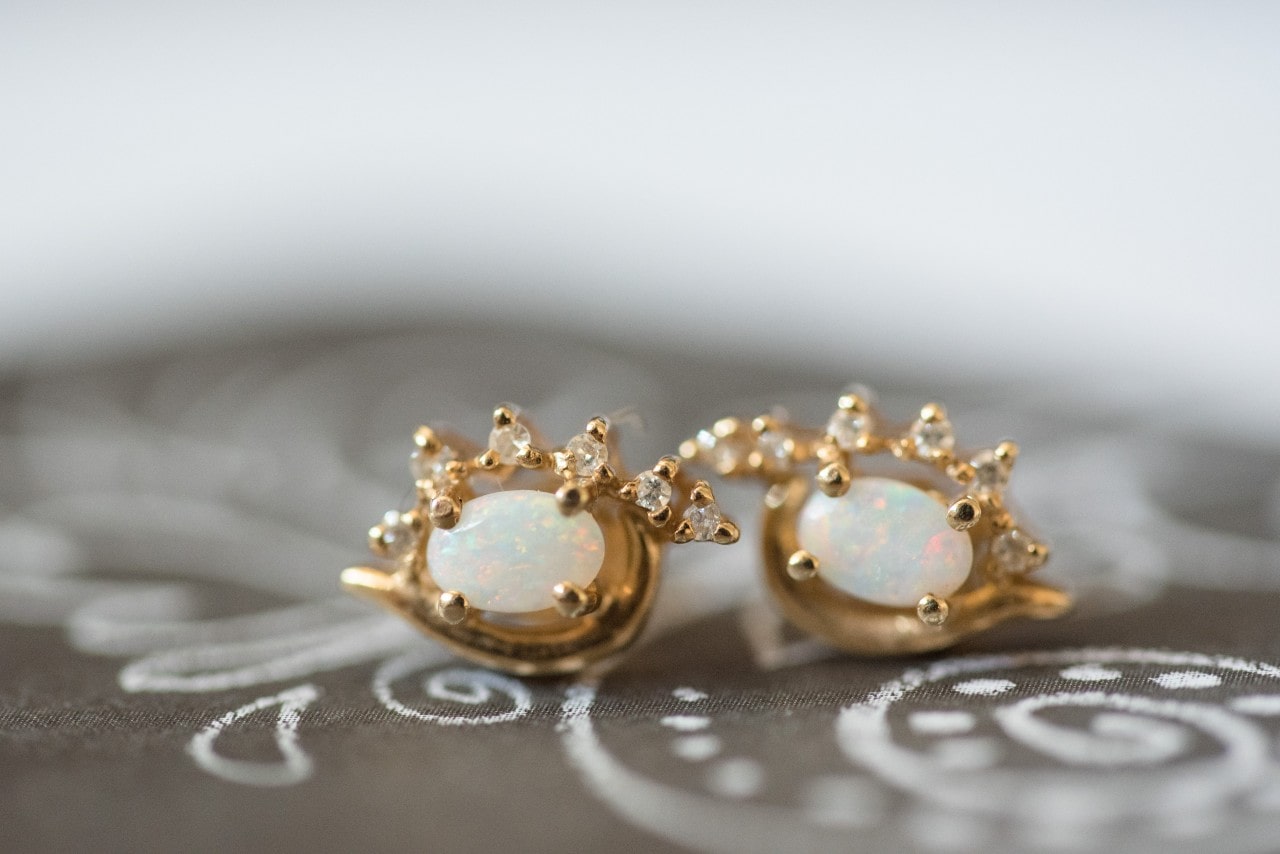 A pair of opal gold stud earrings sit on a painted gray fabric.
