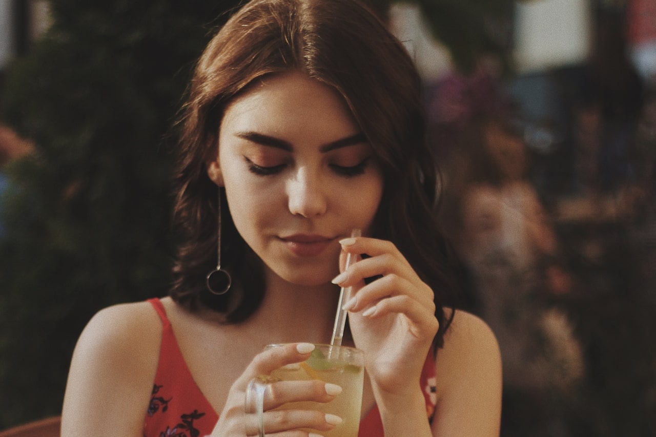 A woman sipping a lemonade wears drop earrings in a cafe.