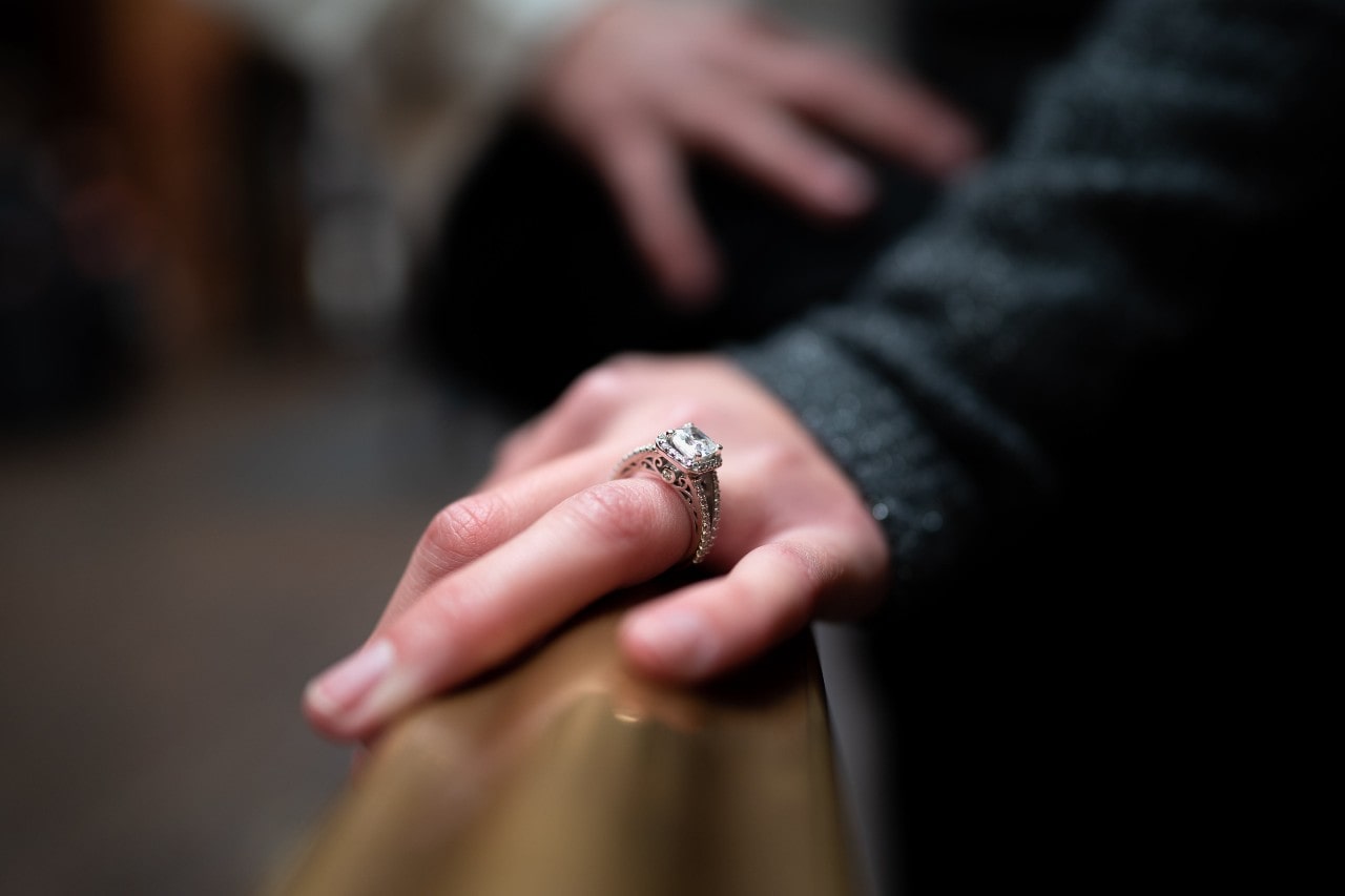 A woman with a vintage-inspired emerald cut ring rests her hand on a rail.