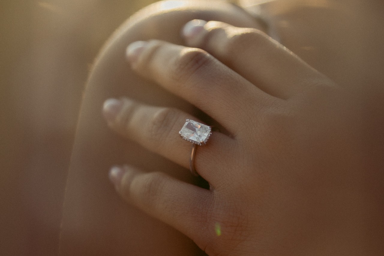 A closeup of an emerald cut engagement ring on a woman’s finger.