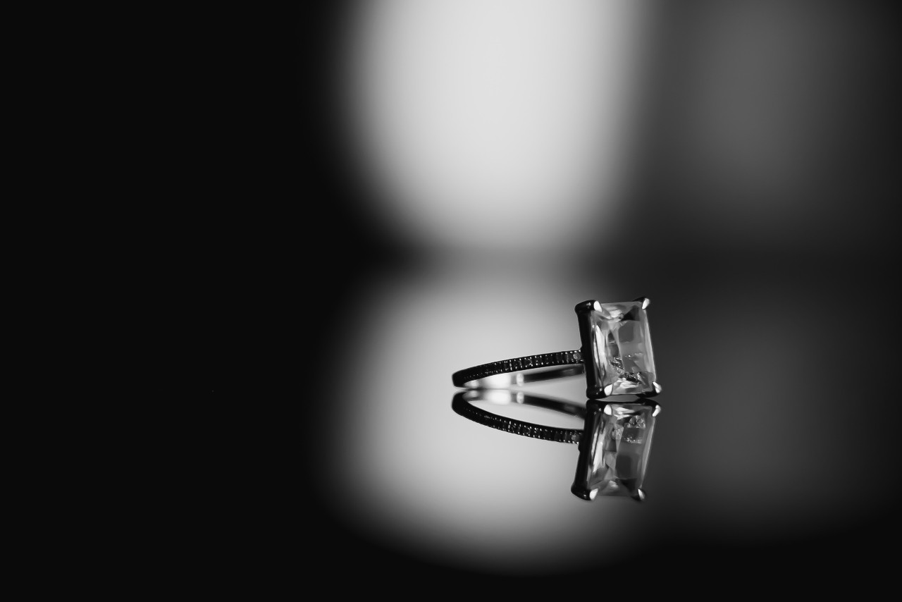 A solitaire emerald cut diamond engagement ring with diamonds along the dainty band