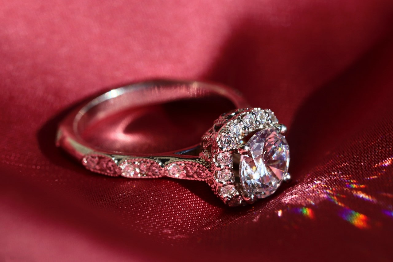 A sparkling diamond ring with a large central stone surrounded by smaller gems rests on red satin fabric.