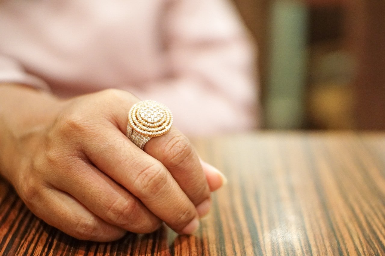 A woman wearing an elaborate gold and diamond fashion ring rests her hand on a table.