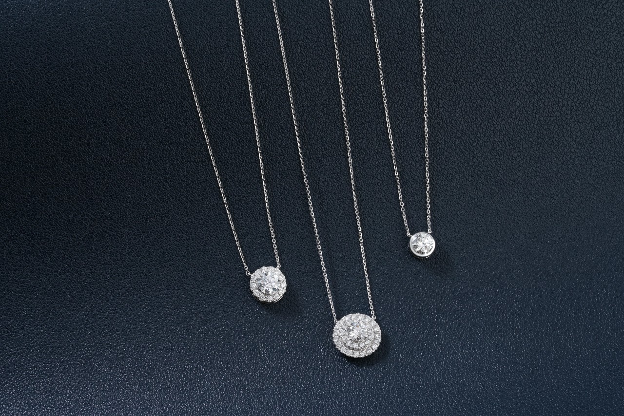 Three silver diamond pendant necklaces on a black textured surface. Three silver diamond pendant necklaces on a black textured surface.