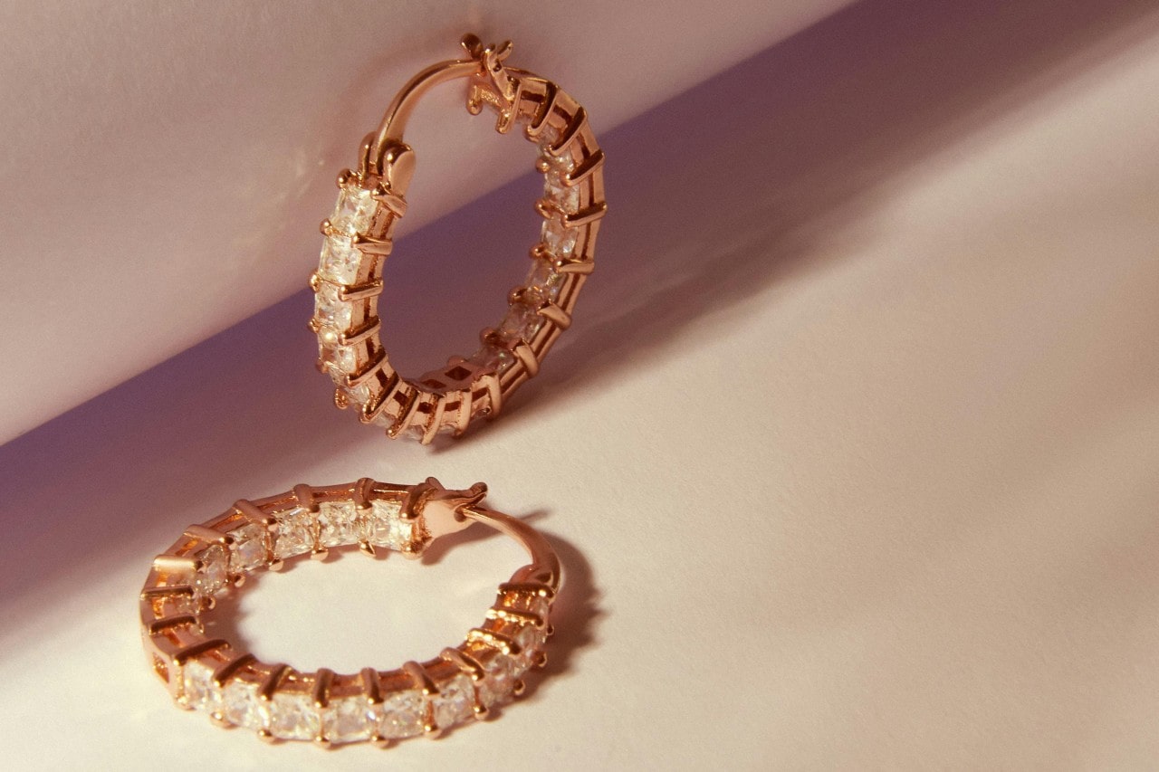 A pair of yellow gold diamond huggie earrings on a beige surface. A pair of yellow gold diamond huggie earrings on a beige surface.