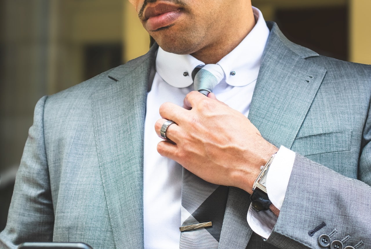 A man in grey suit fixes his tie, showcasing stainless steel wedding band A man in grey suit fixes his tie, showcasing stainless steel wedding band