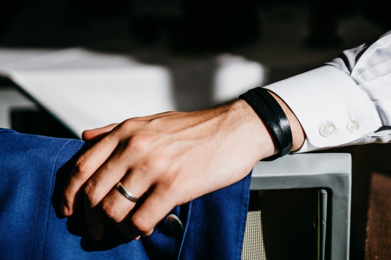 A close up of a man’s hand, showcasing white gold wedding band and rubber black bracelet. A close up of a man’s hand, showcasing white gold wedding band and rubber black bracelet.