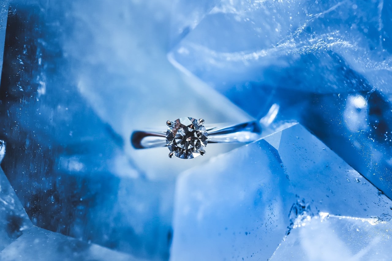 A platinum solitaire engagement ring sits among ice cubes.