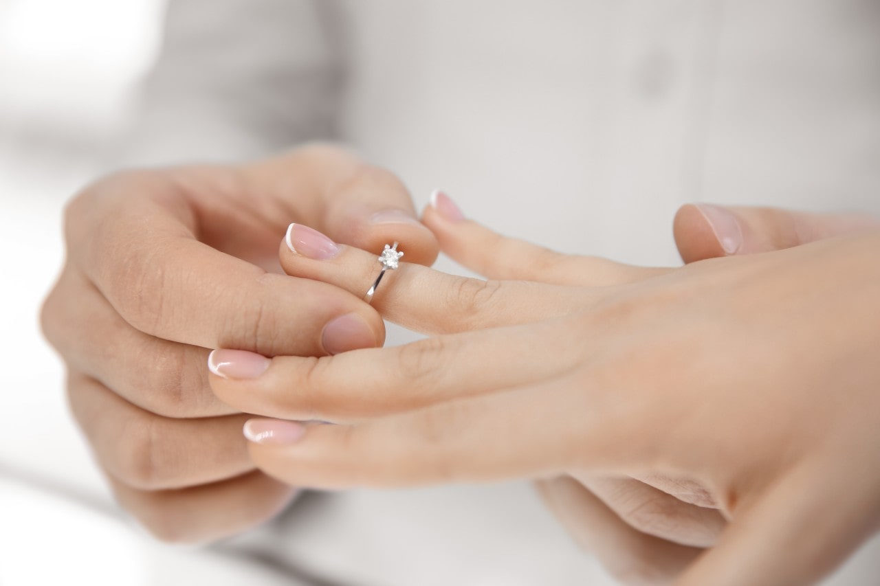 A man slides a minimalist solitaire engagement ring on a woman’s finger.