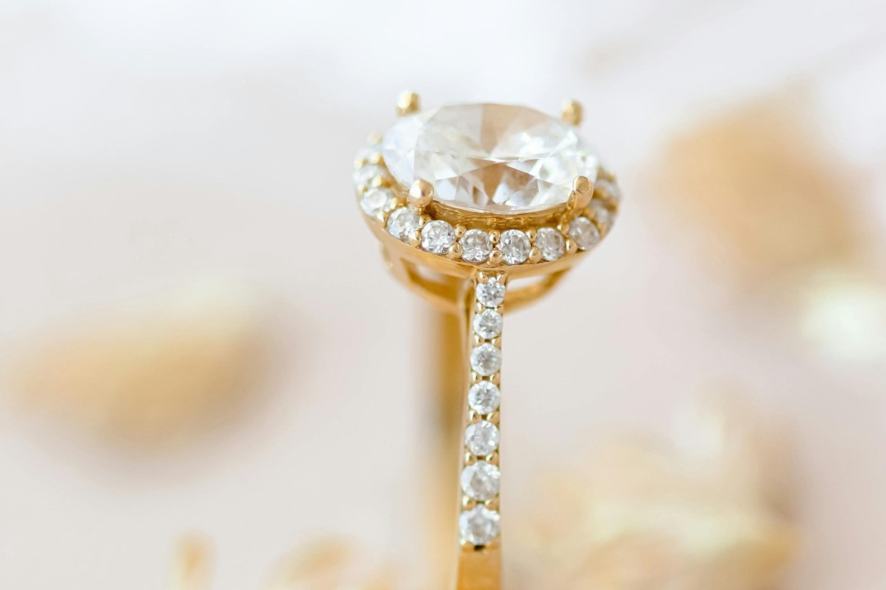 A close-up of a halo gold oval cut halo and side stone engagement ring. A close-up of a halo gold oval cut halo and side stone engagement ring.