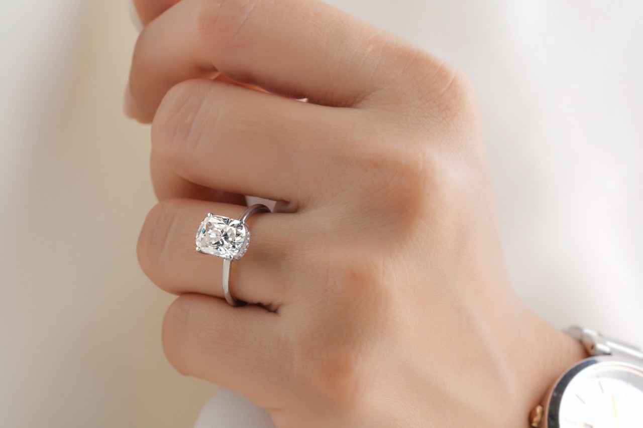 close up image of a woman’s hand wearing a white gold solitaire engagement ring