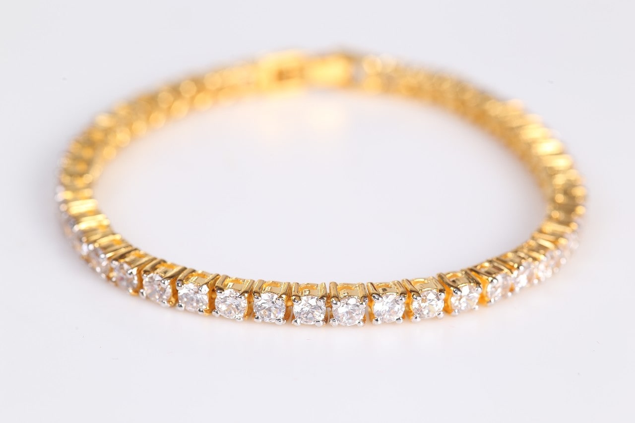 a yellow gold diamond tennis bracelet on a plain white surface