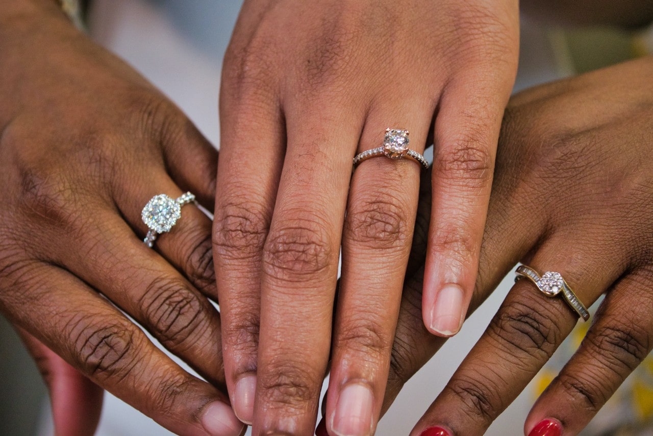 three hands wearing engagement rings of varying styles