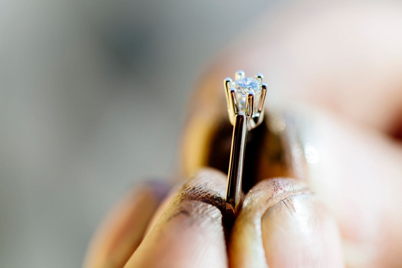 A close-up of a gold solitaire diamond engagement ring held by jeweler’s fingers A close-up of a gold solitaire diamond engagement ring held by jeweler’s fingers
