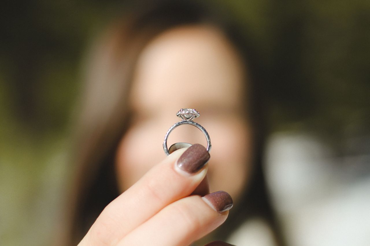 A woman with blurred facial features holds up a solitaire diamond engagement ring A woman with blurred facial features holds up a solitaire diamond engagement ring